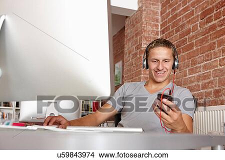 Young man at work using mp3 player View Large Photo Image Picture - Young man at work using mp3 player. Fotosearch