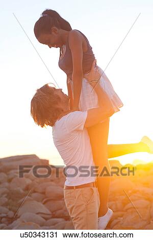 Stock Image - Young man lifting girlfriend at sunset. Fotosearch