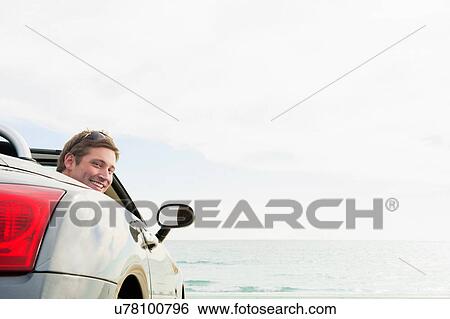 Stock Photograph - Young man sitting in convertible sports car. Fotosearch