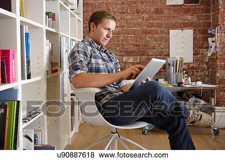 Young man sitting on chair using digital tablet View Large Photo Image Stock Photo - Young man sitting on chair using digital tablet. Fotosearch