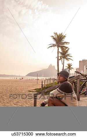 Stock Image - Young man sitting on steps on Ipanema Beach, Rio de Janeiro, Brazil. Fotosearch