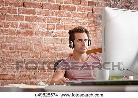 Young man using computer wearing headphones View Large Photo Image Picture - Young man using computer wearing headphones. Fotosearch