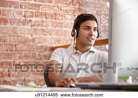 Stock Photography - Young man using computer wearing headphones. Fotosearch