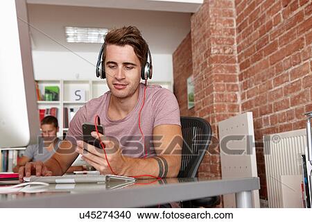 Stock Image - Young man wearing headphones using mp3 player. Fotosearch