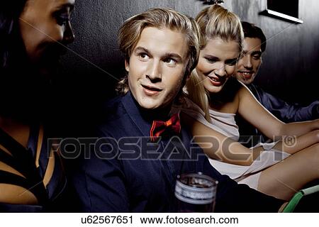 Stock Image - Young men and women sitting together in nightclub. Fotosearch