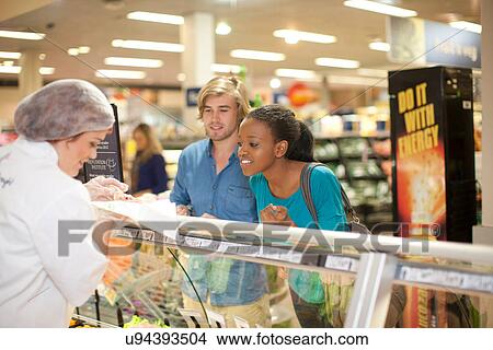 Young sales assistant at counter with customers View Large Photo Image Picture - Young sales assistant at counter with customers. Fotosearch
