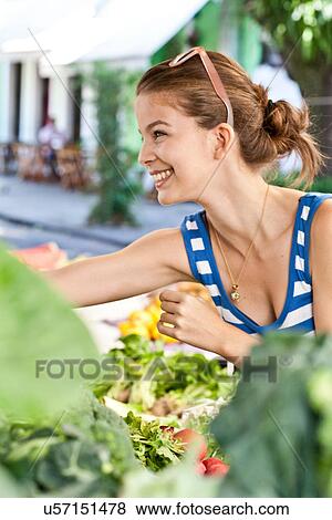 Stock Photo - Young woman buying vegetables in market. Fotosearch