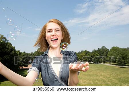 Stock Image - Young woman having fun with bubbles in park. Fotosearch