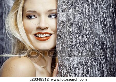 Stock Image - Young woman hiding behind silver curtain. Fotosearch