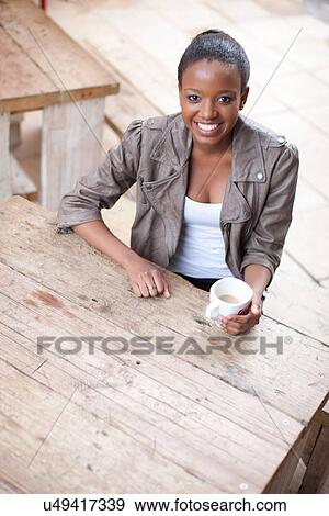Stock Photo - Young woman holding coffee cup in street cafe. Fotosearch