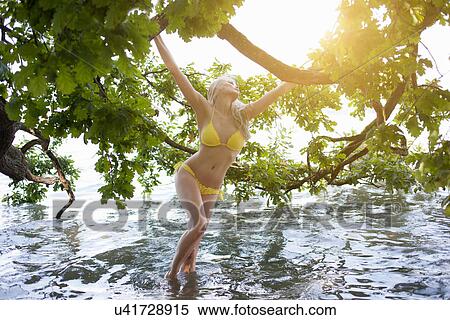 Stock Photography - Young woman in lake holding tree branch. Fotosearch