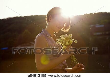 Stock Photography - Young woman in meadow holding bunch of wild flowers. Fotosearch