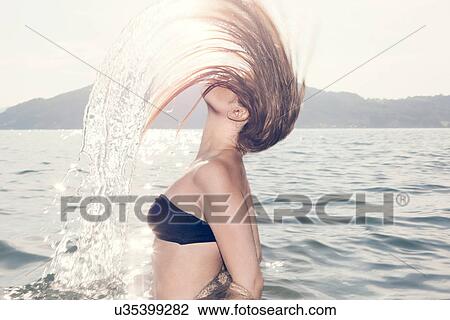 Stock Image - Young woman in sea throwing head back. Fotosearch