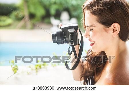 Stock Image - Young woman looking through camera viewfinder. Fotosearch