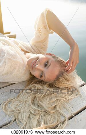 Stock Image - Young woman lying on lake pier. Fotosearch