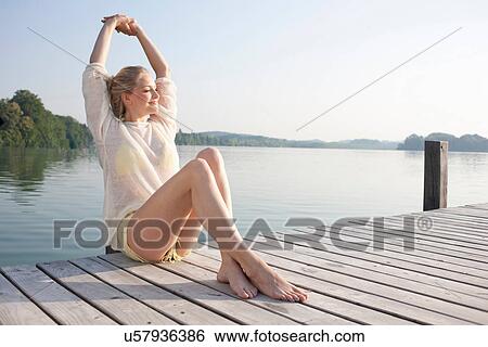 Stock Photograph - Young woman relaxing on lake pier. Fotosearch