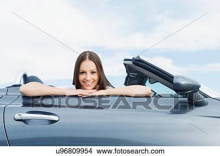 Picture - Young woman sitting in convertible sports car. Fotosearch