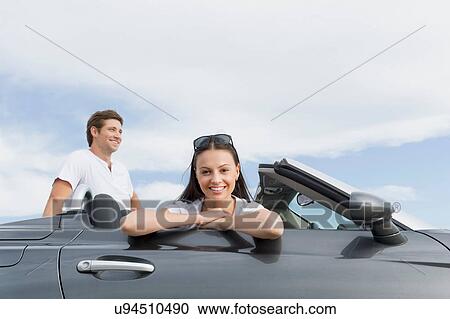 Young woman sitting in convertible sports car, boyfriend behind View Large Photo Image Stock Image - Young woman sitting in convertible sports car, boyfriend behind. Fotosearch