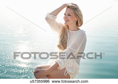 Stock Photograph - Young woman sitting next to lake. Fotosearch