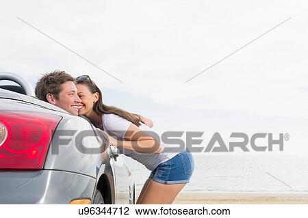 Stock Image - Young woman standing beside convertible sports car, boyfriend sitting in car. Fotosearch