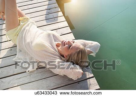 Young woman sunbathing on lake pier View Large Photo Image Stock Image - Young woman sunbathing on lake pier. Fotosearch