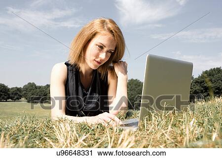 Stock Image - Young woman using laptop in park. Fotosearch