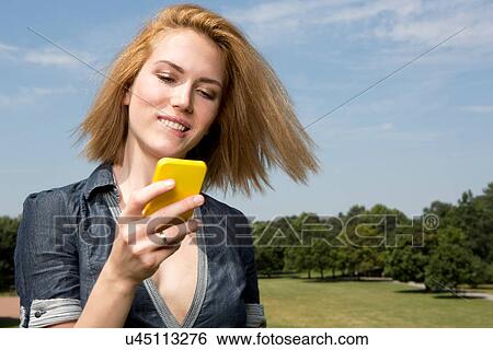 Young woman using smartphone in park View Large Photo Image Stock Photograph - Young woman using smartphone in park. Fotosearch