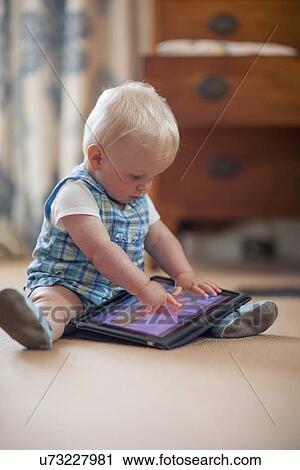 Stock Image - Baby boy (12-17 months) playing with digital tablet. Fotosearch