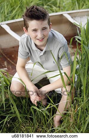 Boy (12-13) crouching on grass near boat View Large Photo Image Stock Image - Boy (12-13) crouching on grass near boat. Fotosearch