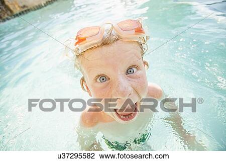 Stock Image - Boy (4-5) swimming in swimming pool and making funny face. Fotosearch