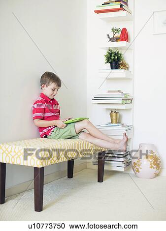 Stock Image - Boy (6-7) sitting on bench using digital tablet. Fotosearch