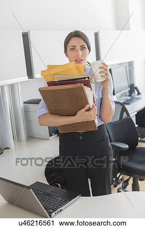 Stock Image - Business woman holding stack of documents in office. Fotosearch