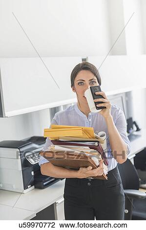 Stock Image - Business woman holding stack of documents and drinking coffee. Fotosearch