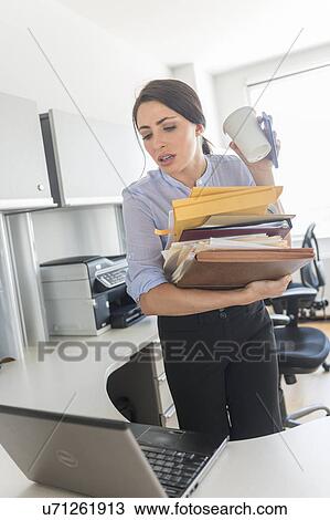 Stock Image - Business woman holding stack of documents and coffee cup. Fotosearch