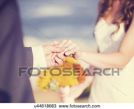 Stock Image - Close up of bride and groom holding hands. Fotosearch
