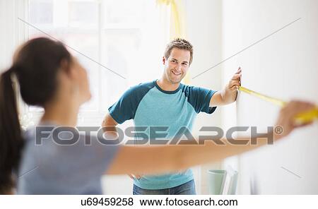Couple measuring wall in their flat View Large Photo Image Stock Photo - Couple measuring wall in their flat. Fotosearch