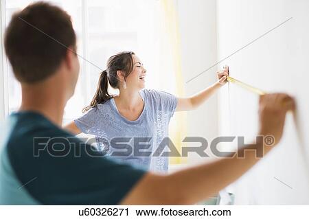 Stock Image - Couple measuring wall. Fotosearch