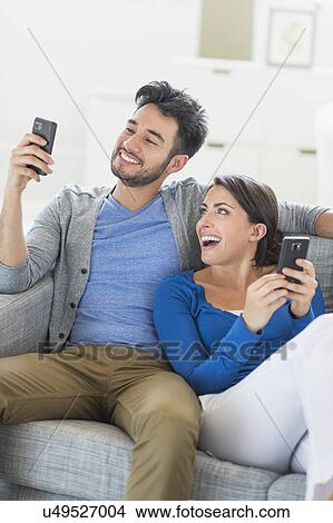 Couple relaxing on sofa with cell phones View Large Photo Image Picture - Couple relaxing on sofa with cell phones. Fotosearch
