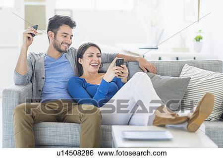 Stock Photograph - Couple relaxing on sofa with cell phones. Fotosearch