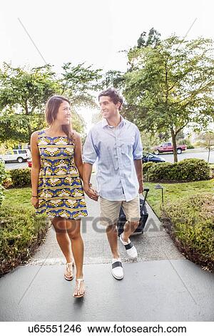 Stock Photograph - Couple walking, man pulling suitcase. Fotosearch