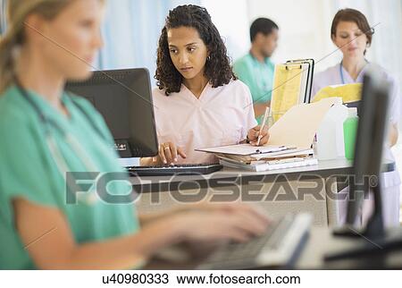 Stock Image - Doctors and nurses working at desks in hospital. Fotosearch