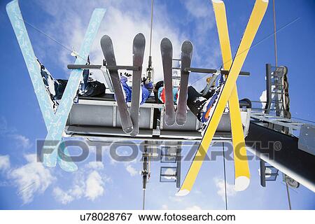 Stock Photo - Family of skiers on ski lift seen from below. Fotosearch