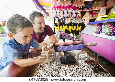 Stock Photo - Father with son (4-5) playing with water gun in amusement park. Fotosearch