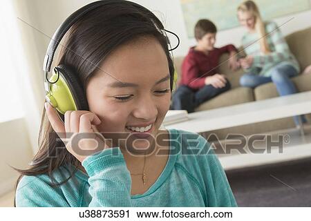 Stock Image - Girl (16-17) listening to music wearing headphones. Fotosearch