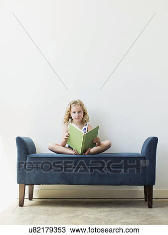Stock Image - Girl (4-5) sitting on bench and reading book. Fotosearch