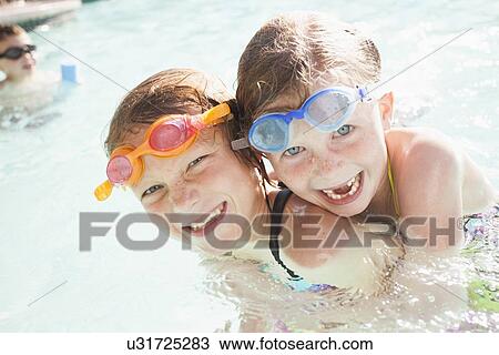Stock Image - Girlfriends (4-5, 8-9) playing in swimming pool. Fotosearch
