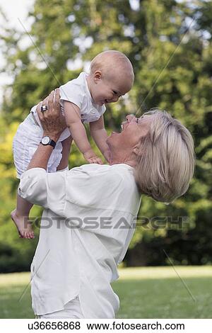 Stock Photo - Grandmother holding her granddaughter (12-17 months) in air. Fotosearch