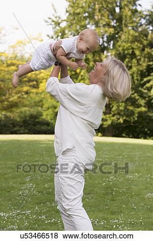 Stock Photo - Grandmother holding her granddaughter (12-17 months) in air. Fotosearch