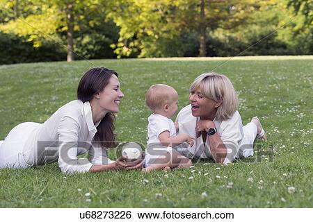 Stock Photograph - Grandmother with mother and granddaughter (12-17 months) playing on grass. Fotosearch