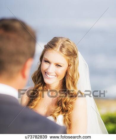 Stock Photo - Groom looking at bride, sea in background. Fotosearch